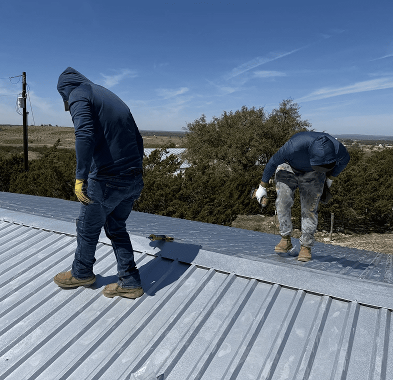 Two men repairing metal rooftop.